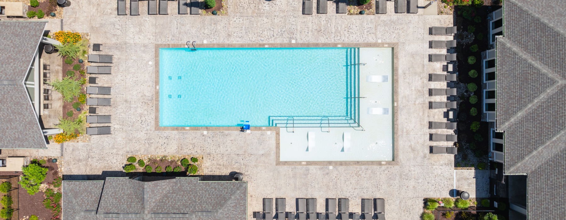 Aerial view of a resort-style swimming pool with tanning ledge, lounge chairs, and landscaped sundeck at a modern apartment community
