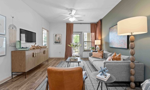 Furnished living room at Pringle Square in Charlotte, NC with a gray couch and orange chair with a door leading out to the balcony.