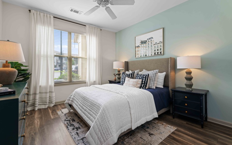 Bright bedroom with large window, modern decor, wood-style flooring, and neutral accents 